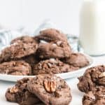 Pecan topped cookies on white plate with milk jug in background.