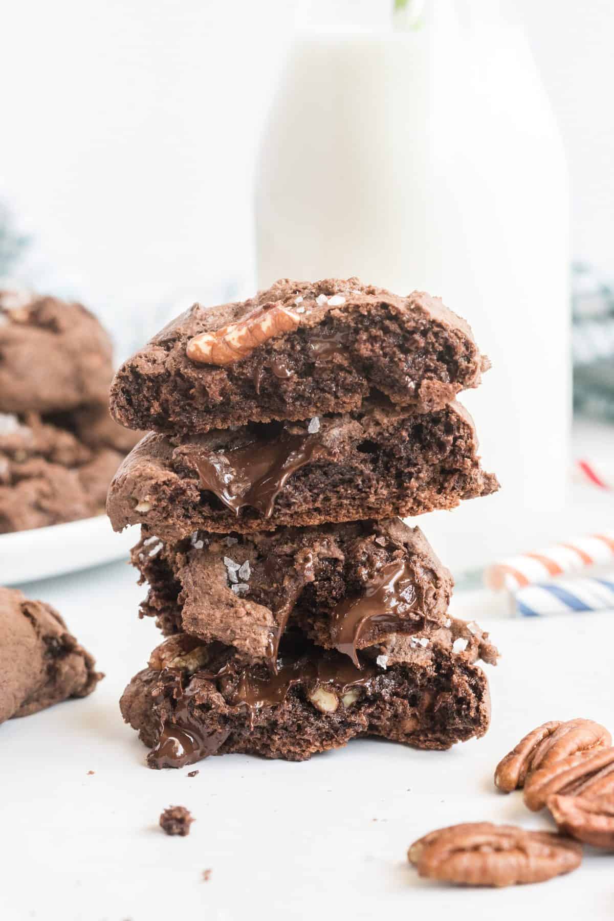 Chocolate cake mix cookies cut in half and stacked, with jug of milk in background.