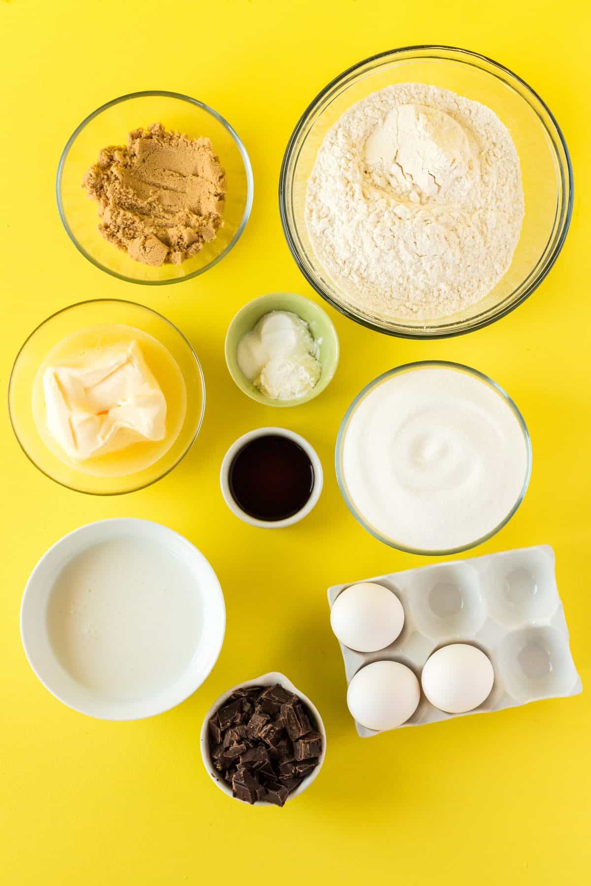 ingredients to make marble cake in small glass bowls on yellow background