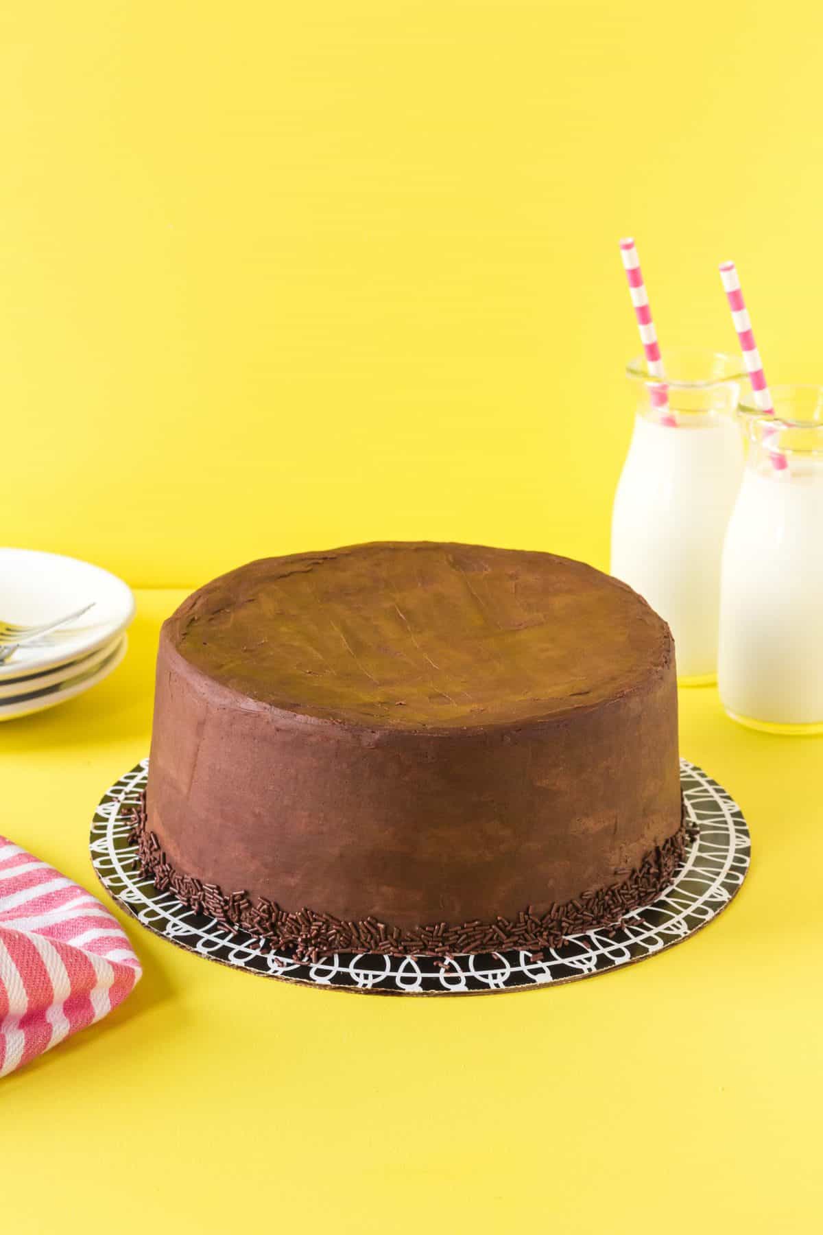 a large chocolate frosted marble cake with two glasses of milk in the background