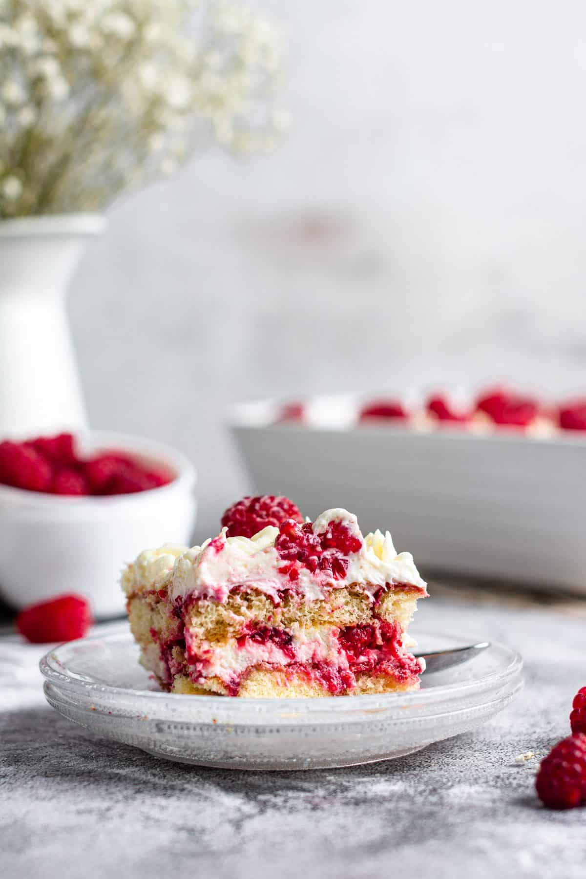slice of raspberry amaretto tiramisu on white plate with bowl of raspberries in the background