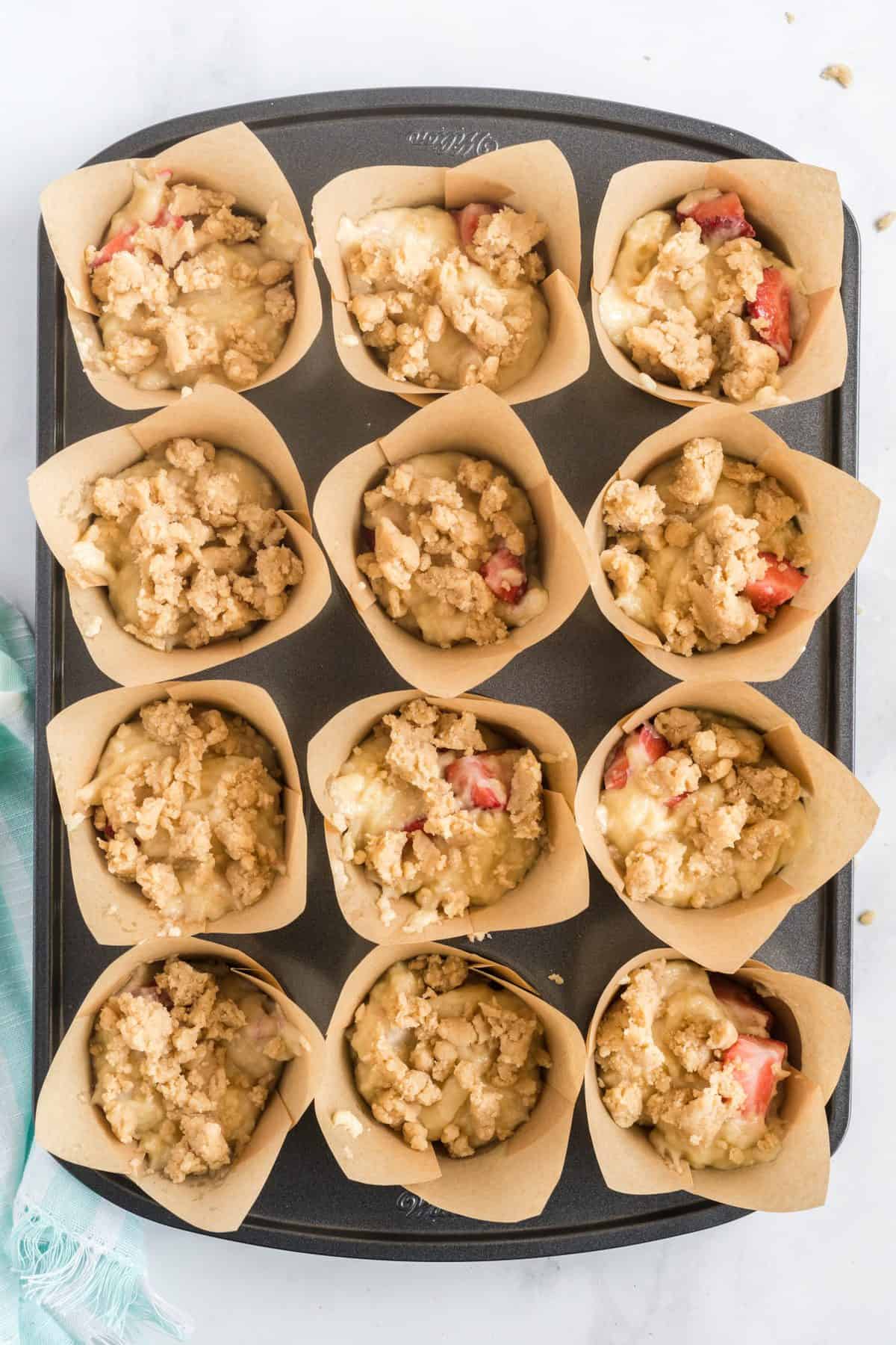 Muffin pan with strawberry muffin batter filled liners. 