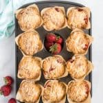 Muffin pan with baked strawberry muffins and fresh strawberries.