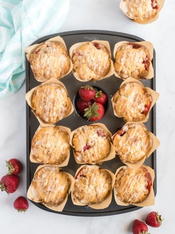 Muffin pan with baked strawberry muffins and fresh strawberries.