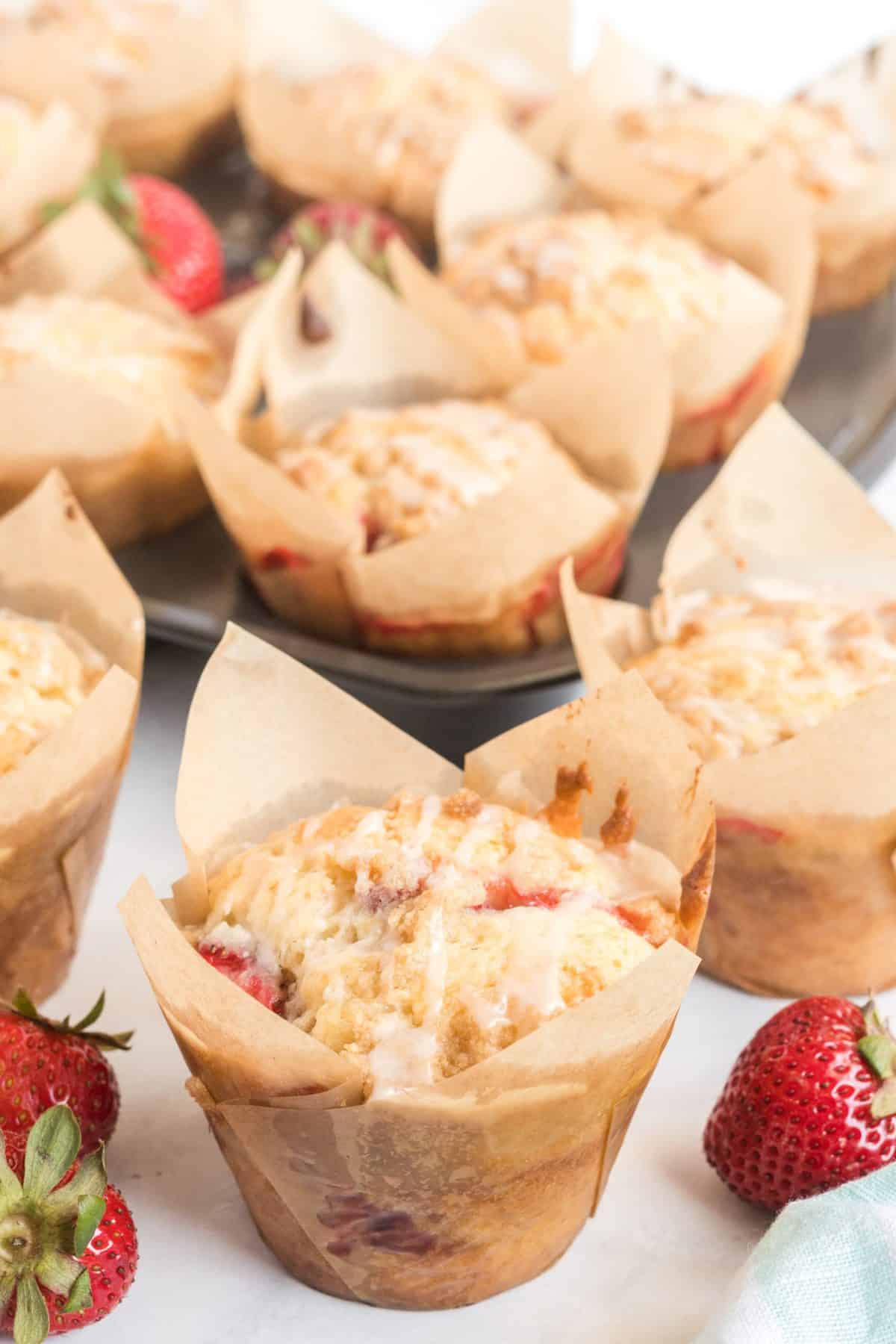 a bunch of strawberry muffins in brown tulip cup liners on white background. 