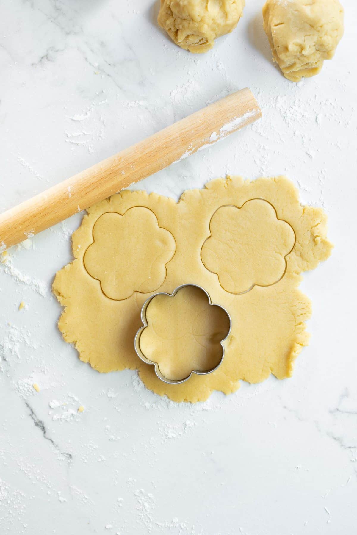 Flower shaped cookie cutter cutting out cookie dough.