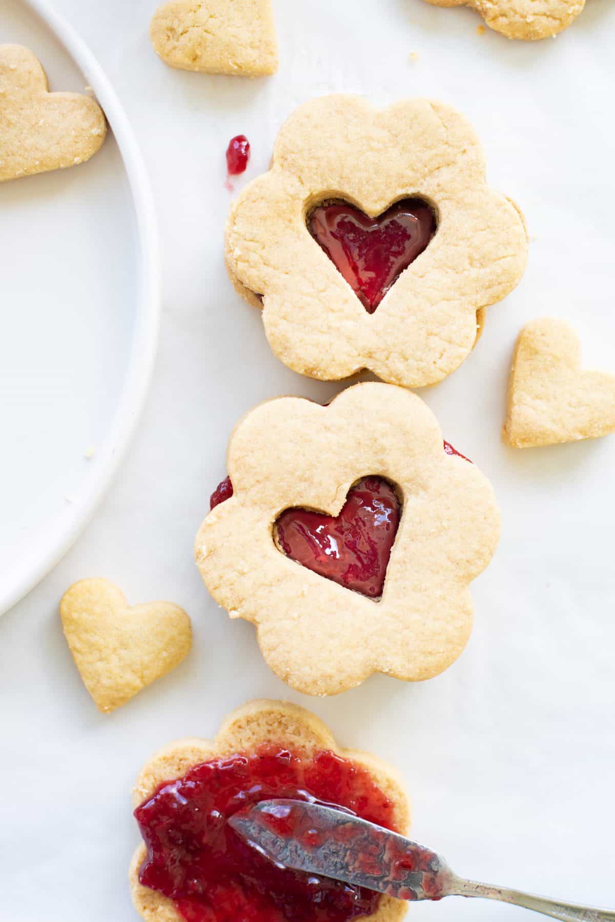Two sandwich heart cookies on white background with a knife and jam. 