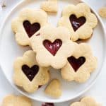 White plate with heart jam filled sugar cookie sandwiches on white background.