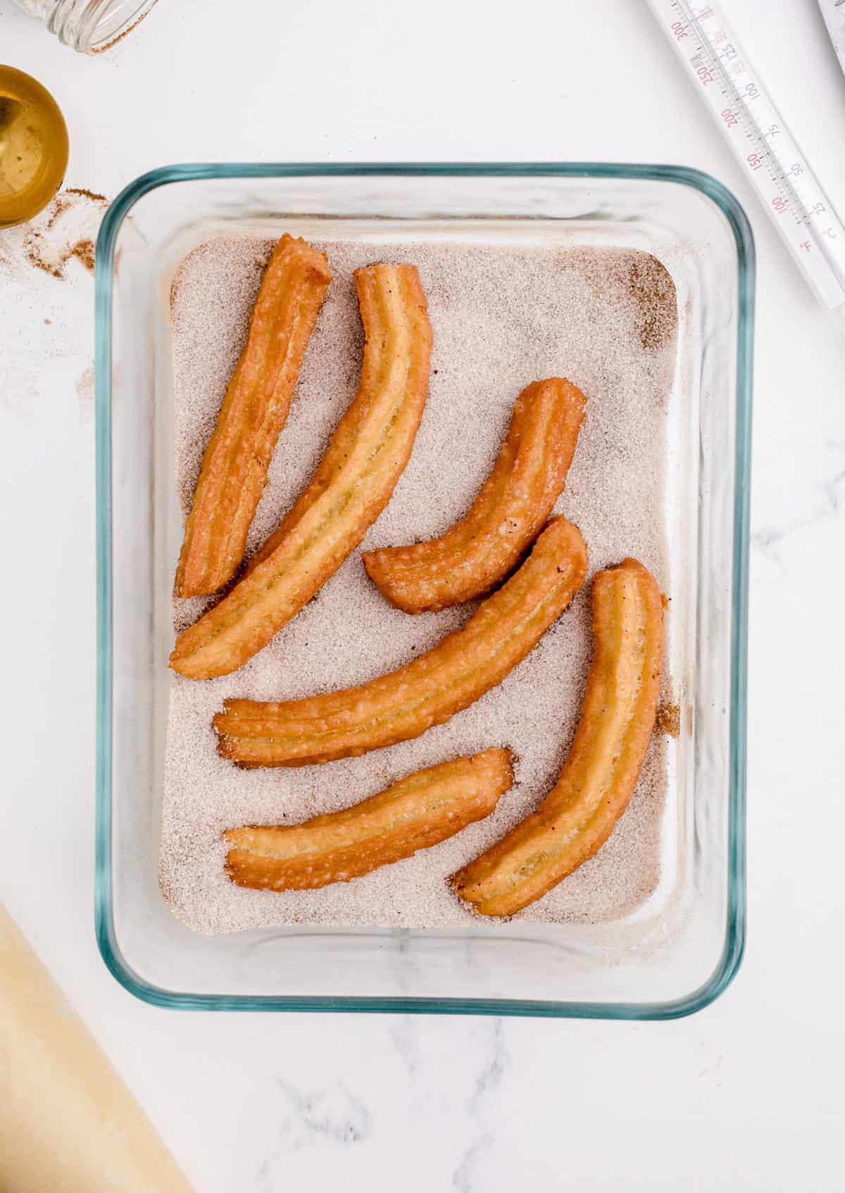 Placing fried churros in pastry dish with cinnamon and sugar. 