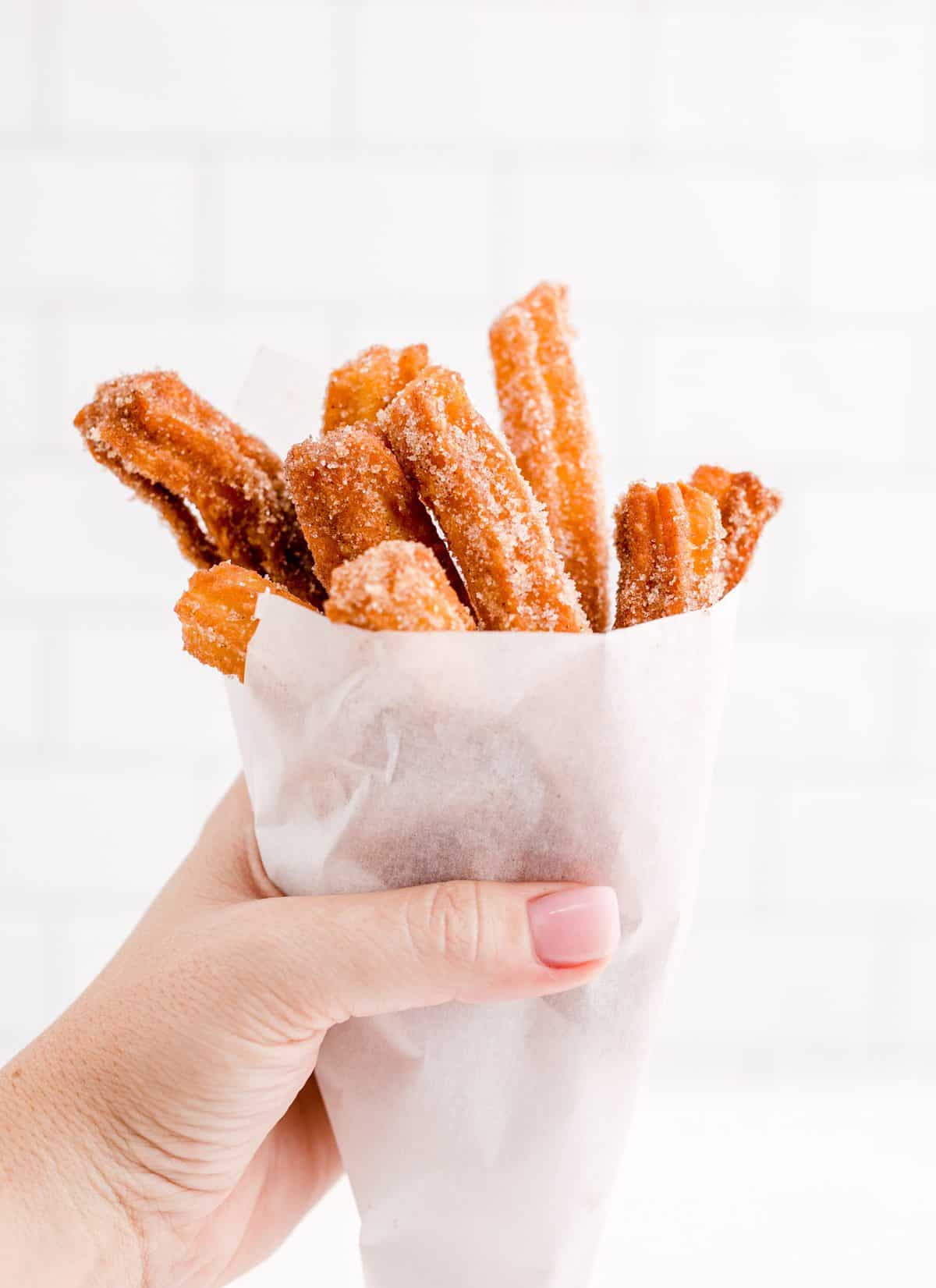 Hand holding a white bag of churros. 