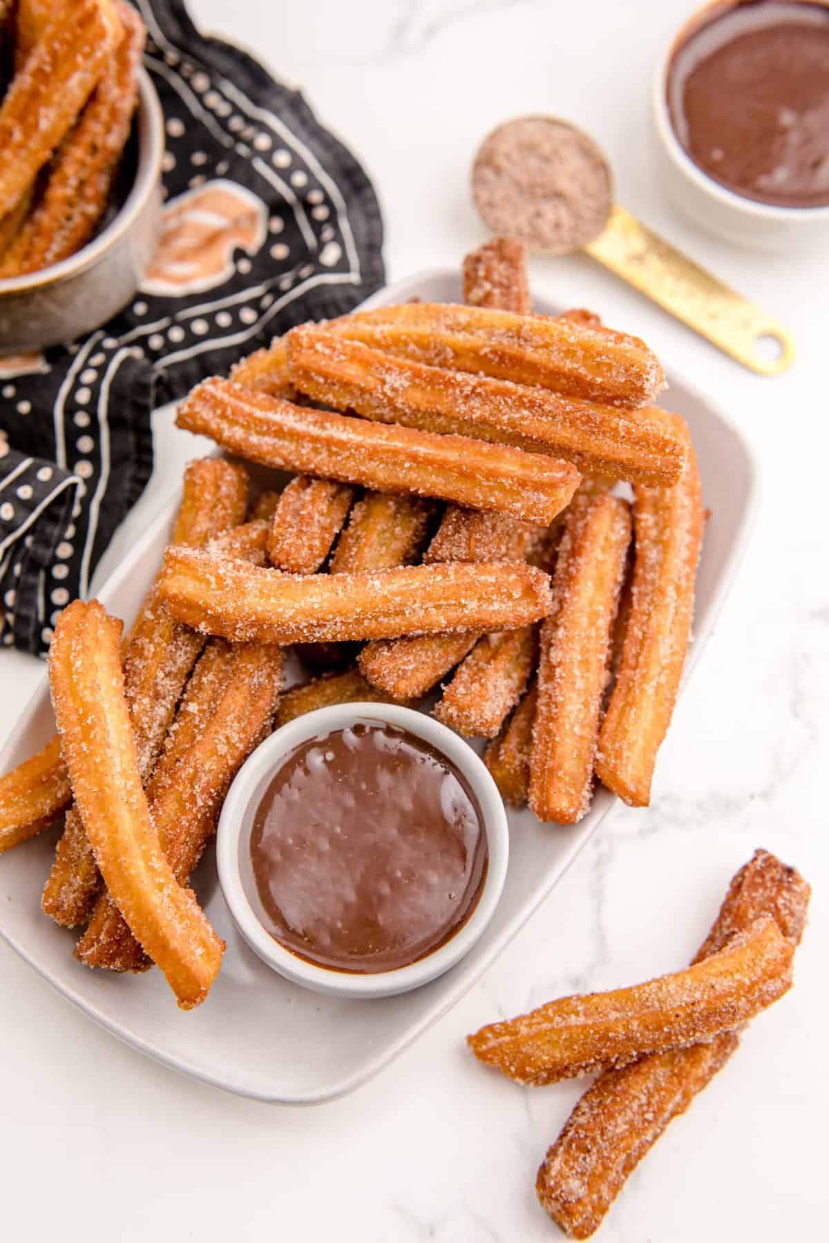 White plate with freshly fried churros and bowl of chocolate sauce.
