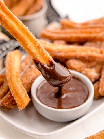churros being dipped in chocolate sauce in white bowl.