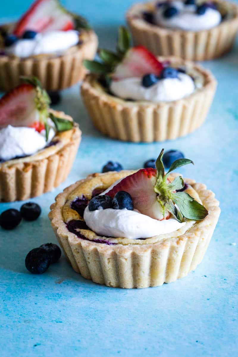 Mini cream cheese berry tarts with whipped cream and strawberries on blue background. 
