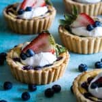 Cream cheese tarts with whipped cream and berries on blue background.