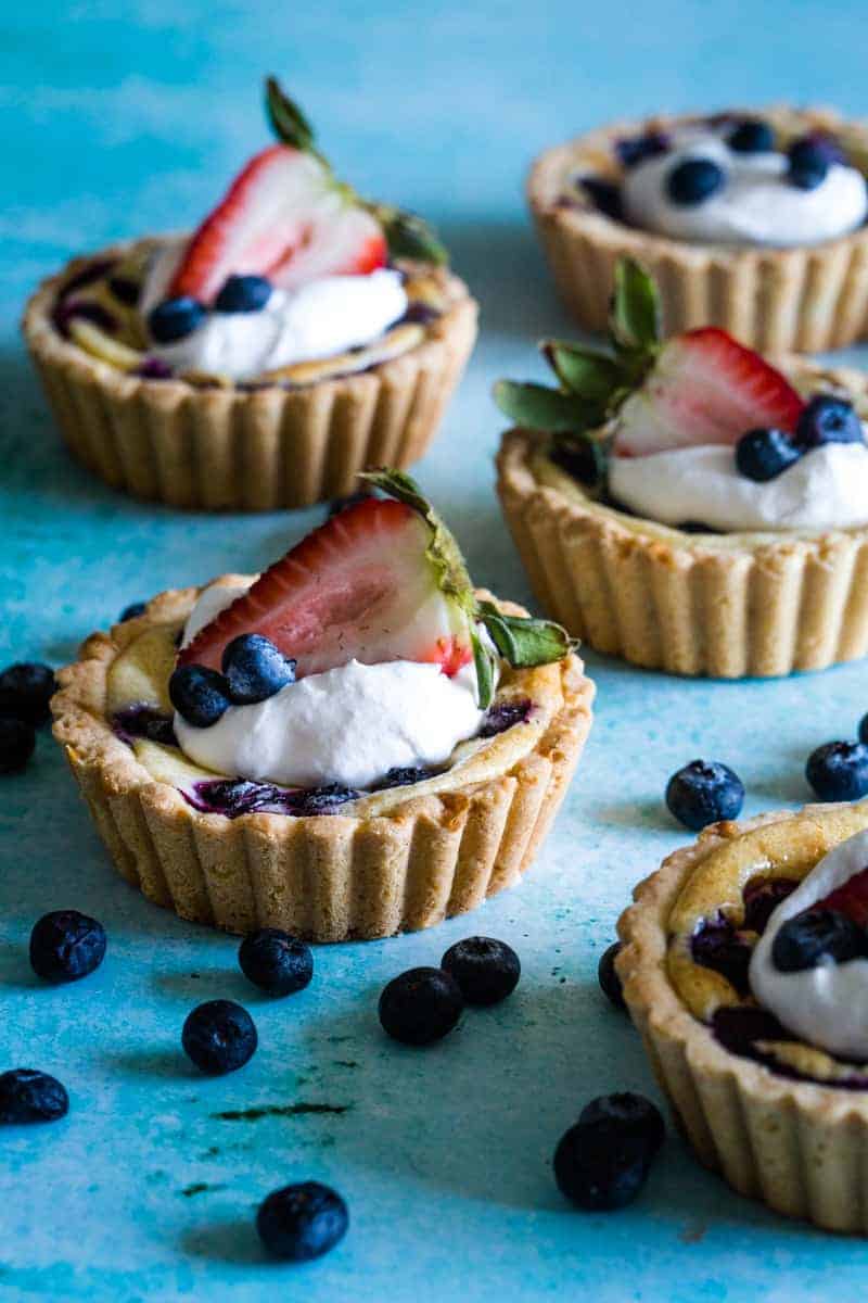 Cream cheese tarts with whipped cream and berries on blue background. 