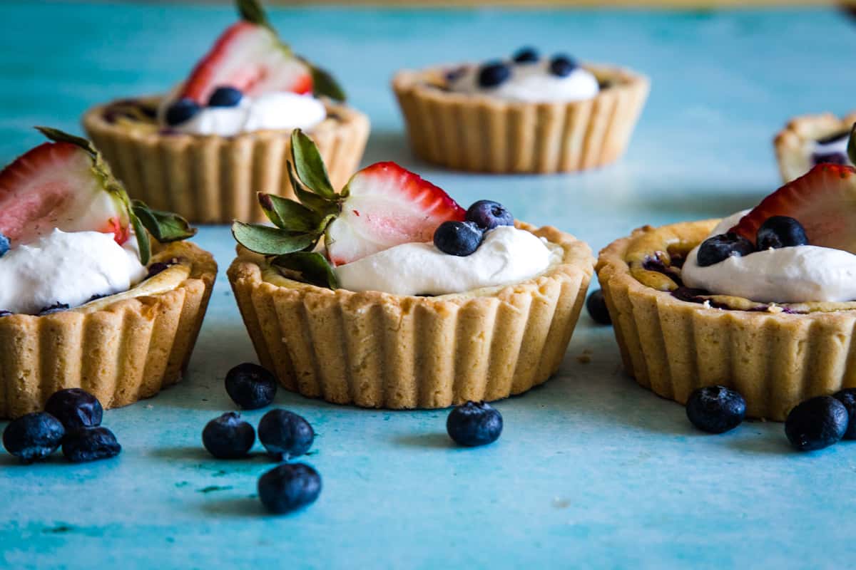 Three tarts lined up on blue background with berries scattered.
