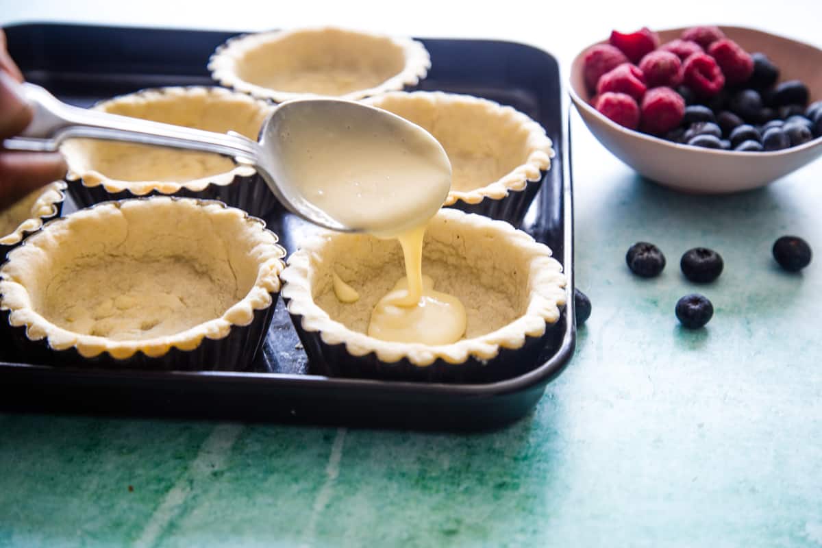 Using a spoon to pour the filling into the tart shells.