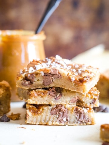 Three stacked cookie bars with jar if dulce de leche in background
