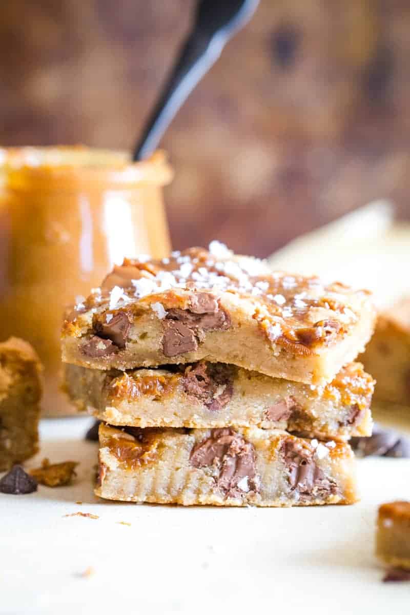Three stacked cookie bars with jar if dulce de leche in background