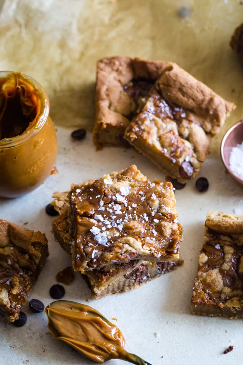 Dulce de leche cookie bars spread out on table with jar of caramel sauce. 