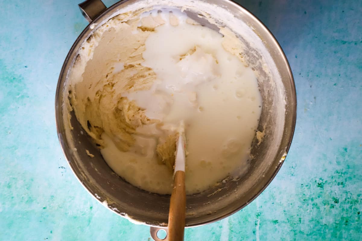 adding coconut milk to cake batter in metal mixing bowl.