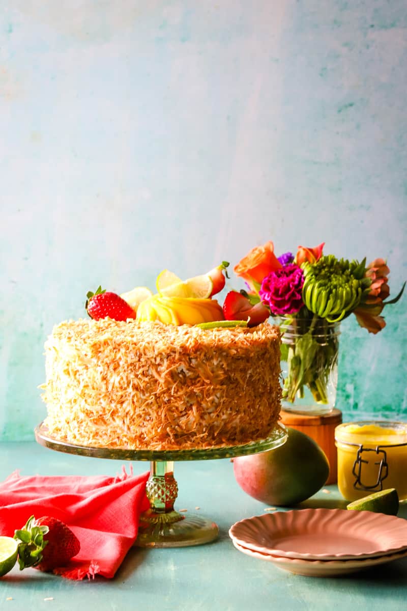 Coconut mango cake with flowers in aground and serving plates. 