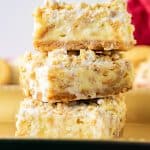 Three cheesecake bars stacked on gold plate.