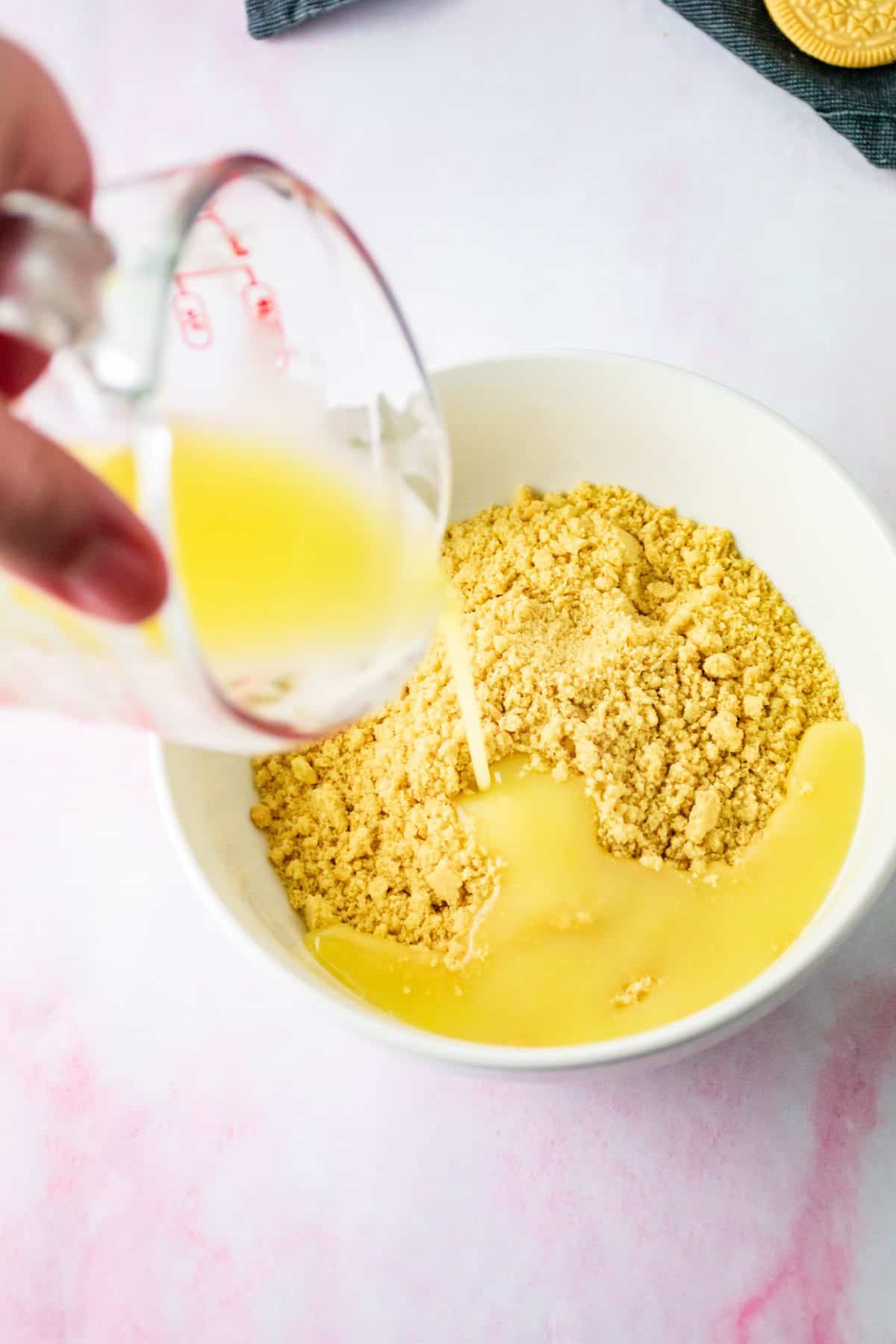 pouring melted butter into bowl with cookie crumbs. 