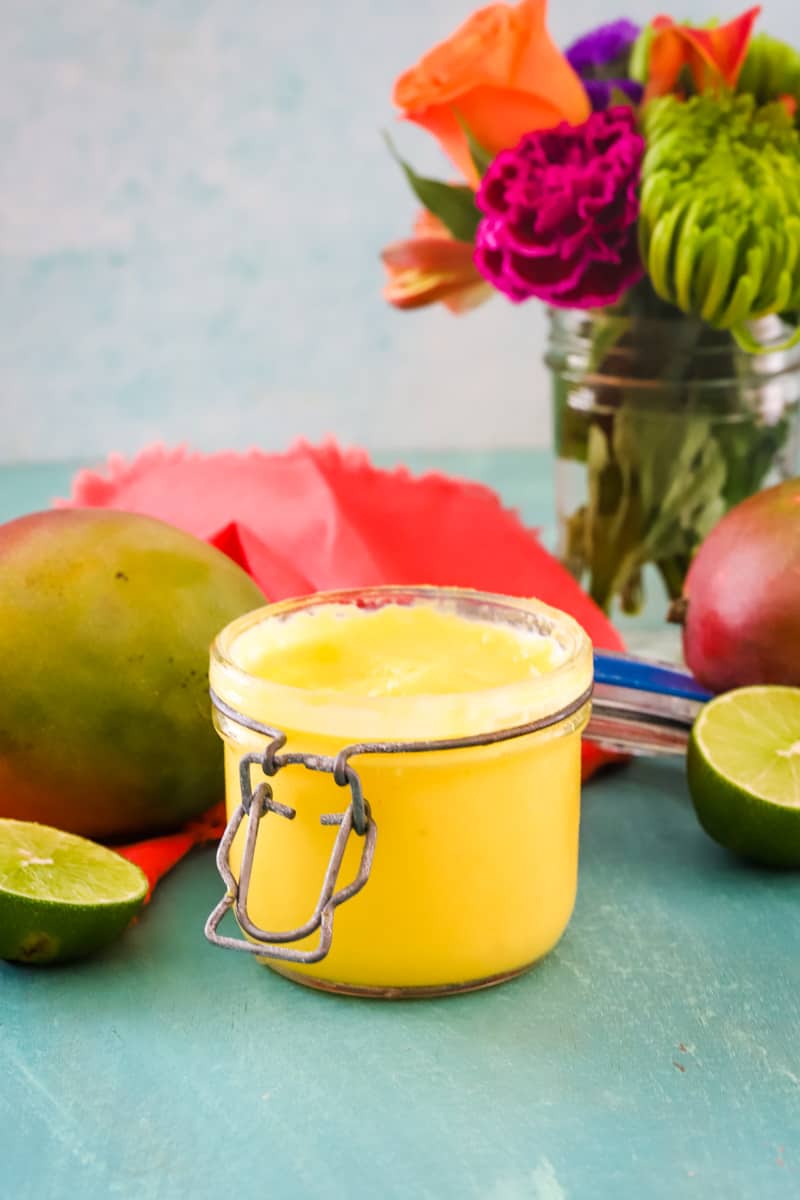 Jar of mango curd with flowers in background. 