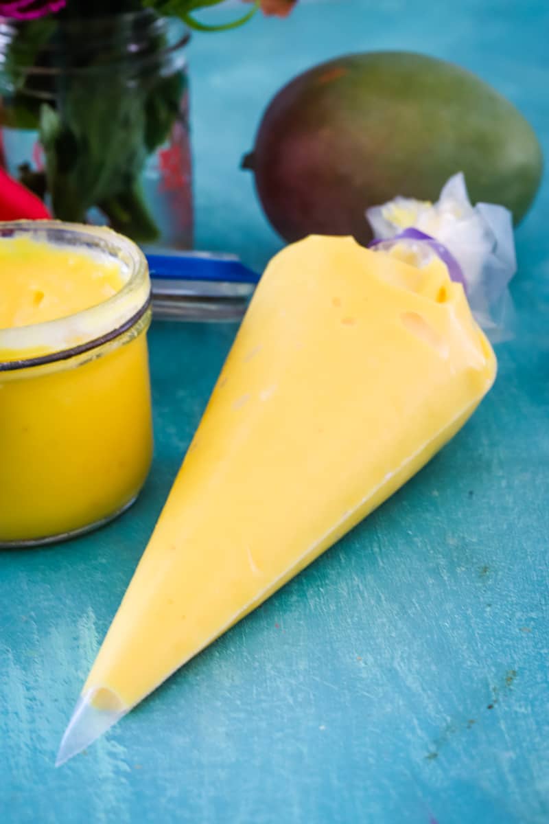 Piping bag full of fresh mango curd on blue table. 