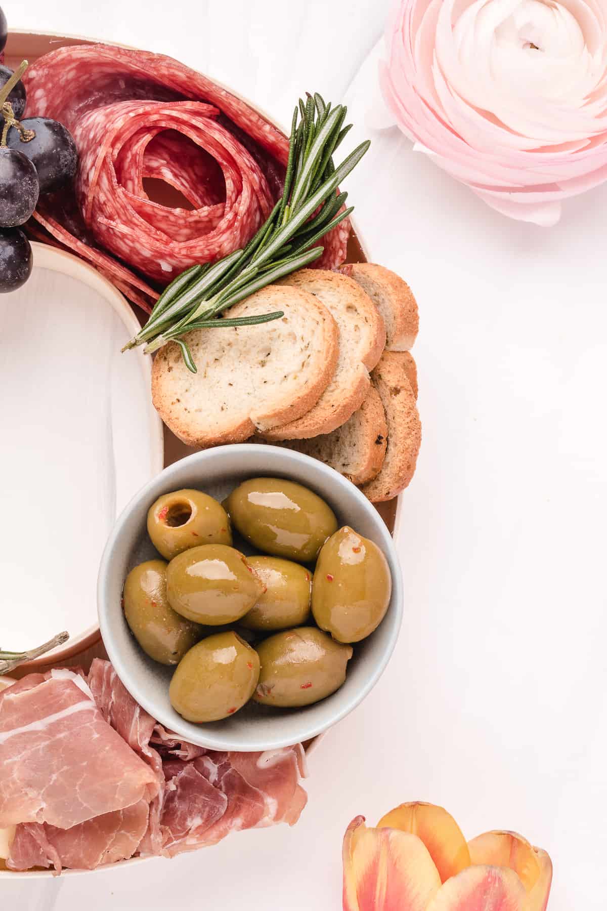 Up close photo of a bowl of olives, bread, and salami. 