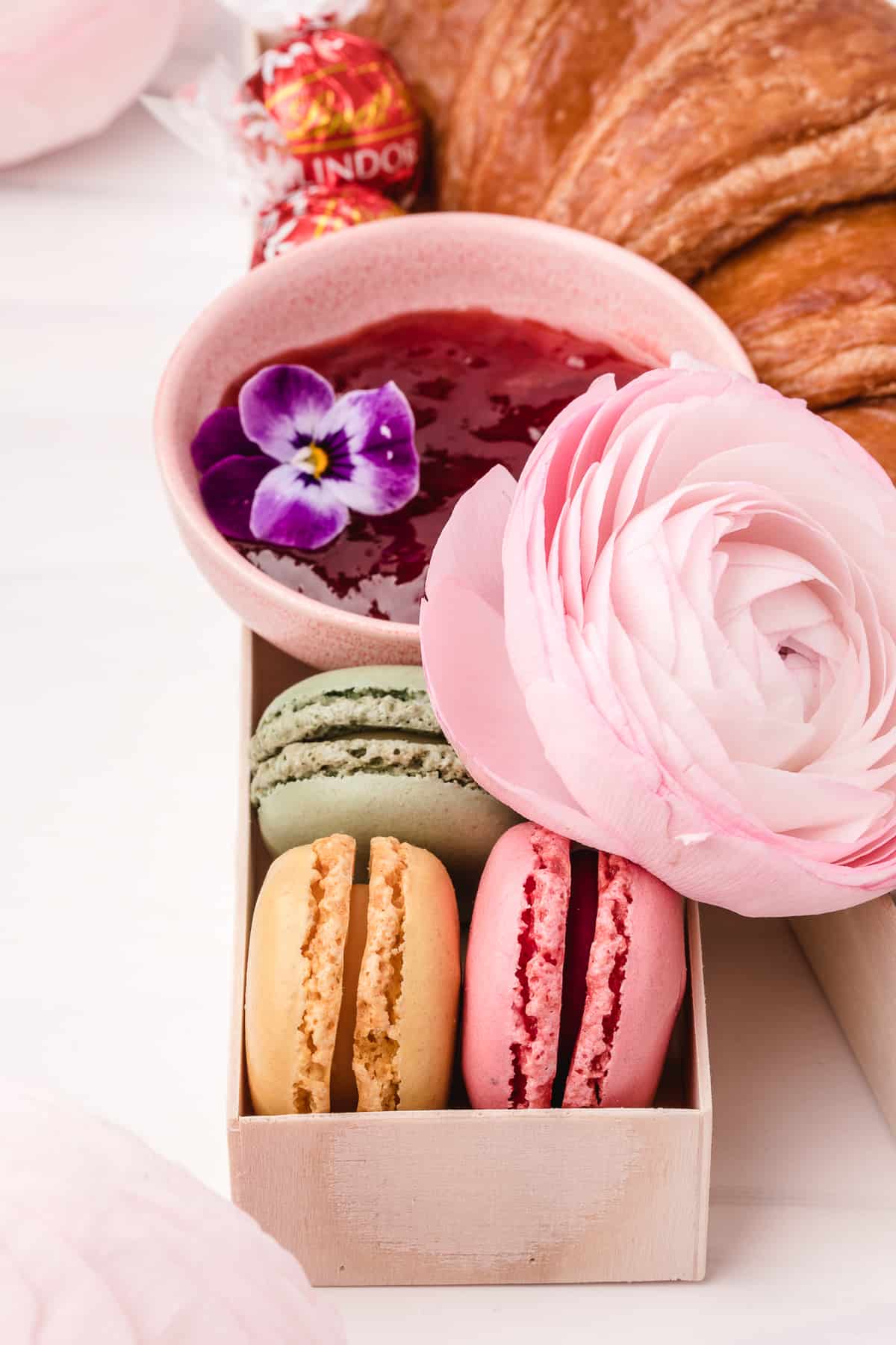 French macarons, flowers, and a bowl of jam on white background. 
