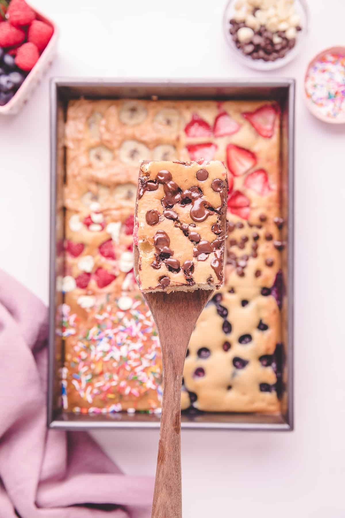 Wooden spoon taking a square of chocolate chip topped sheet pan pancake.