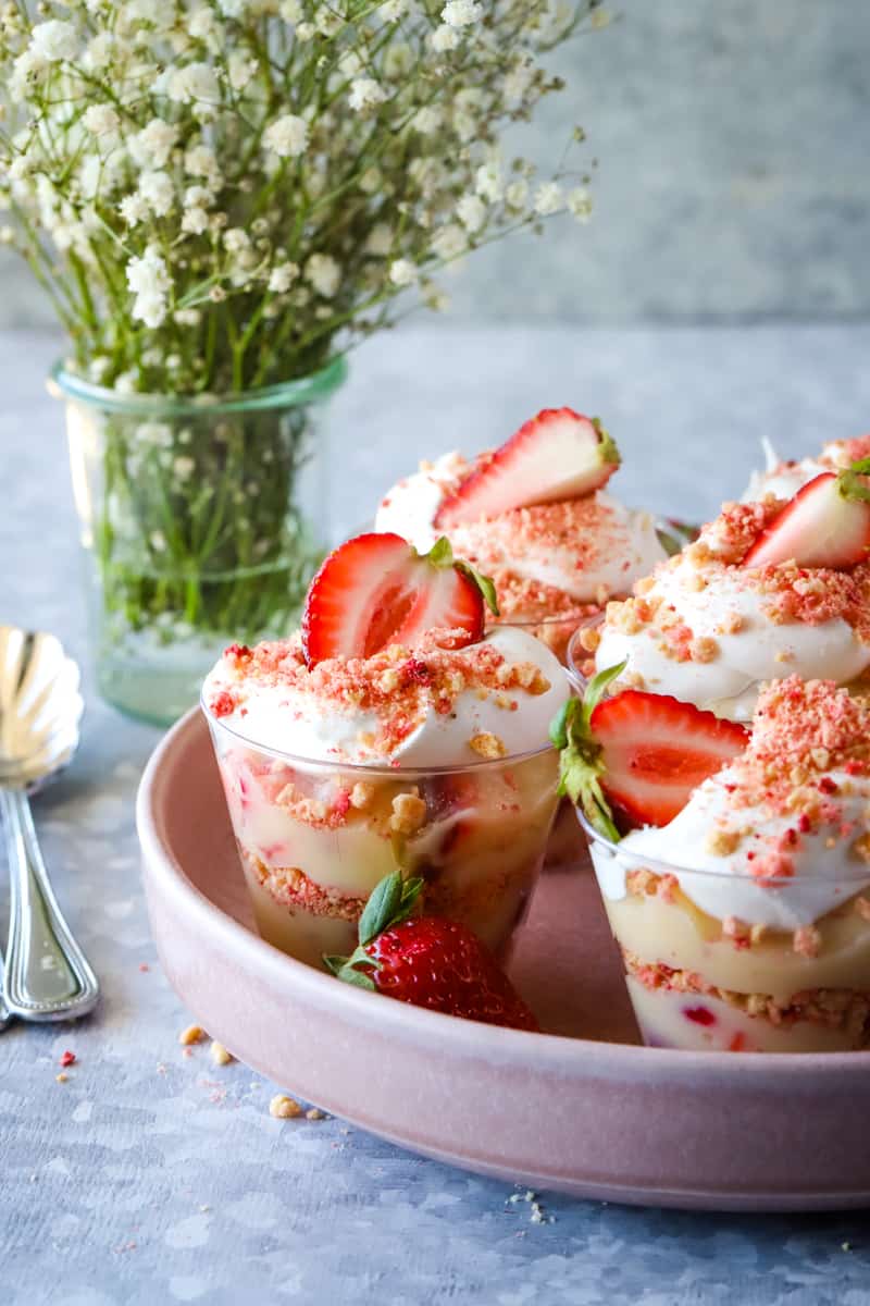 Strawberry pudding cups on pink plate with flowers in the background. 