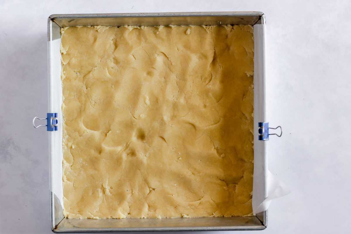 Sugar Cookie Bar dough pressed into the bottom of a lined pan. 