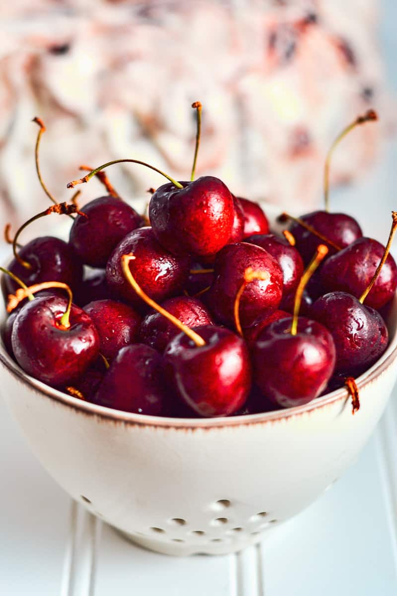 white bowl of fresh cherries on wood background. 