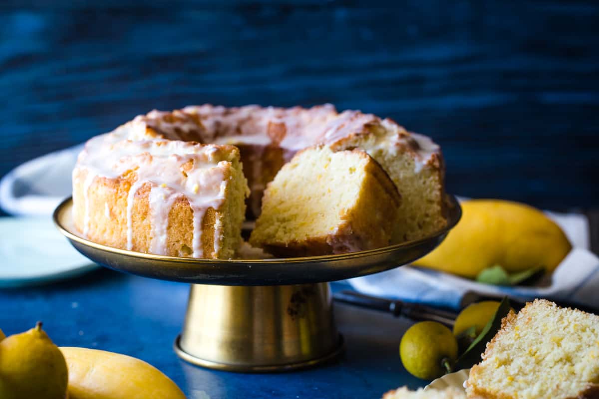 Sliced lemon cake on gold cake plate and blue background. 
