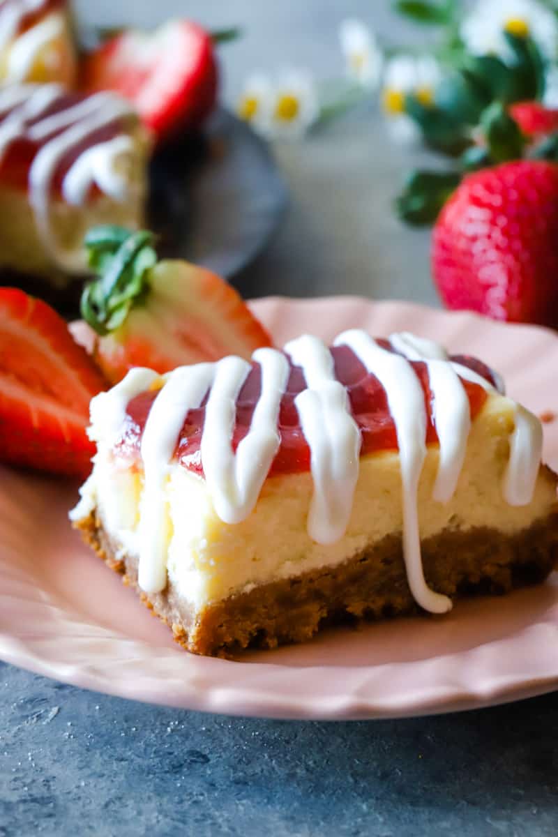 cheesecake bar with sliced strawberries on pink plate. 