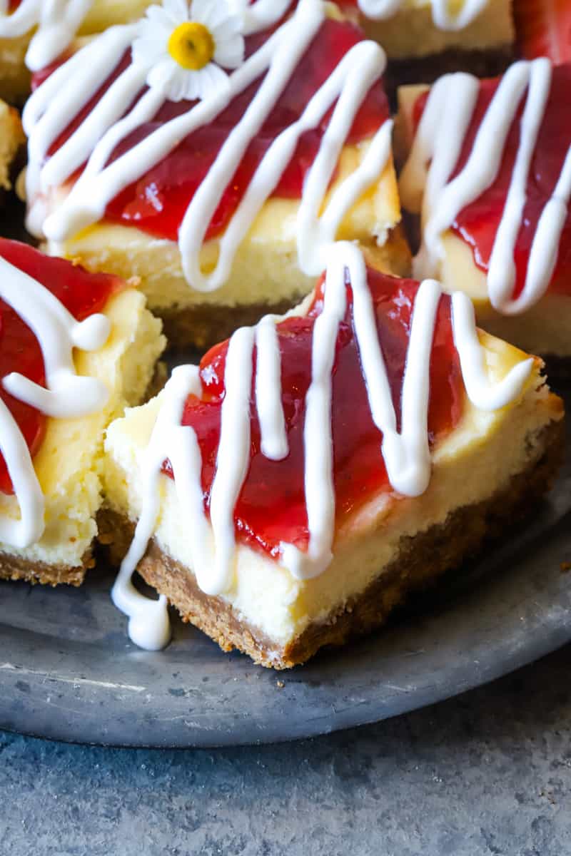 Strawberry cheesecake bars with sour cream drizzle on metal plate. 