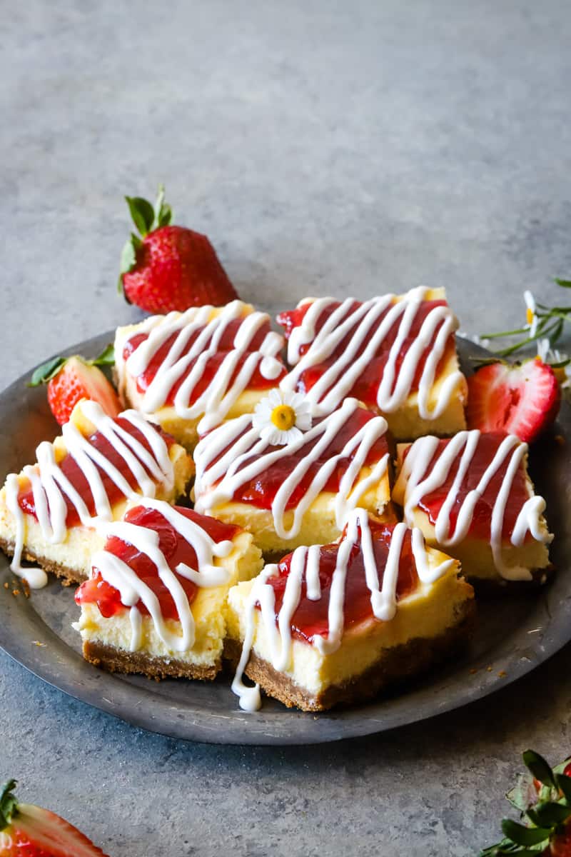 cheesecake bars with fresh strawberries on metal plate and grey background.