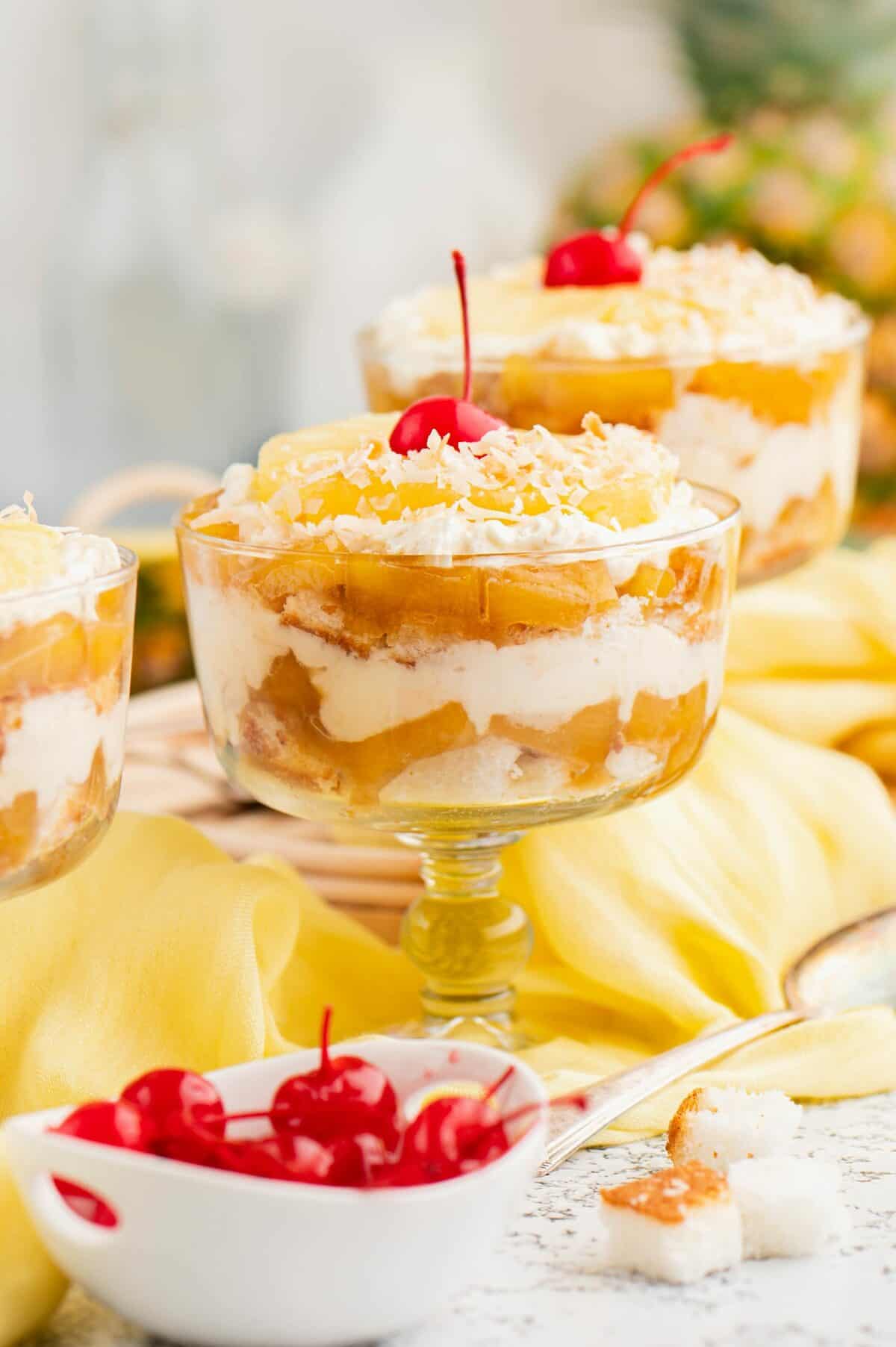 two pineapple cheesecake trifles with bowl of cherries in front. 