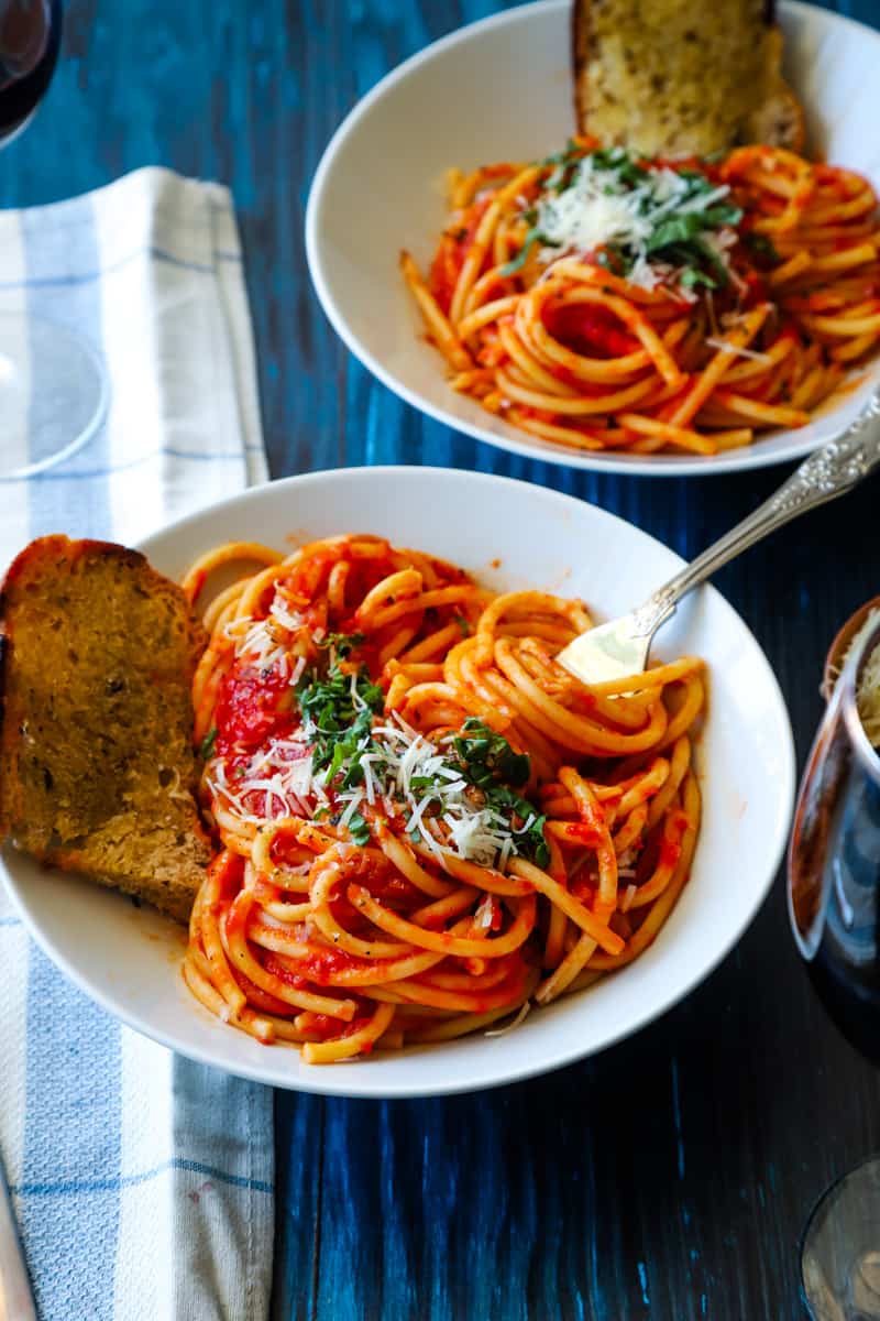 Two white bowls of spaghetti with a fork swirling pasta. 