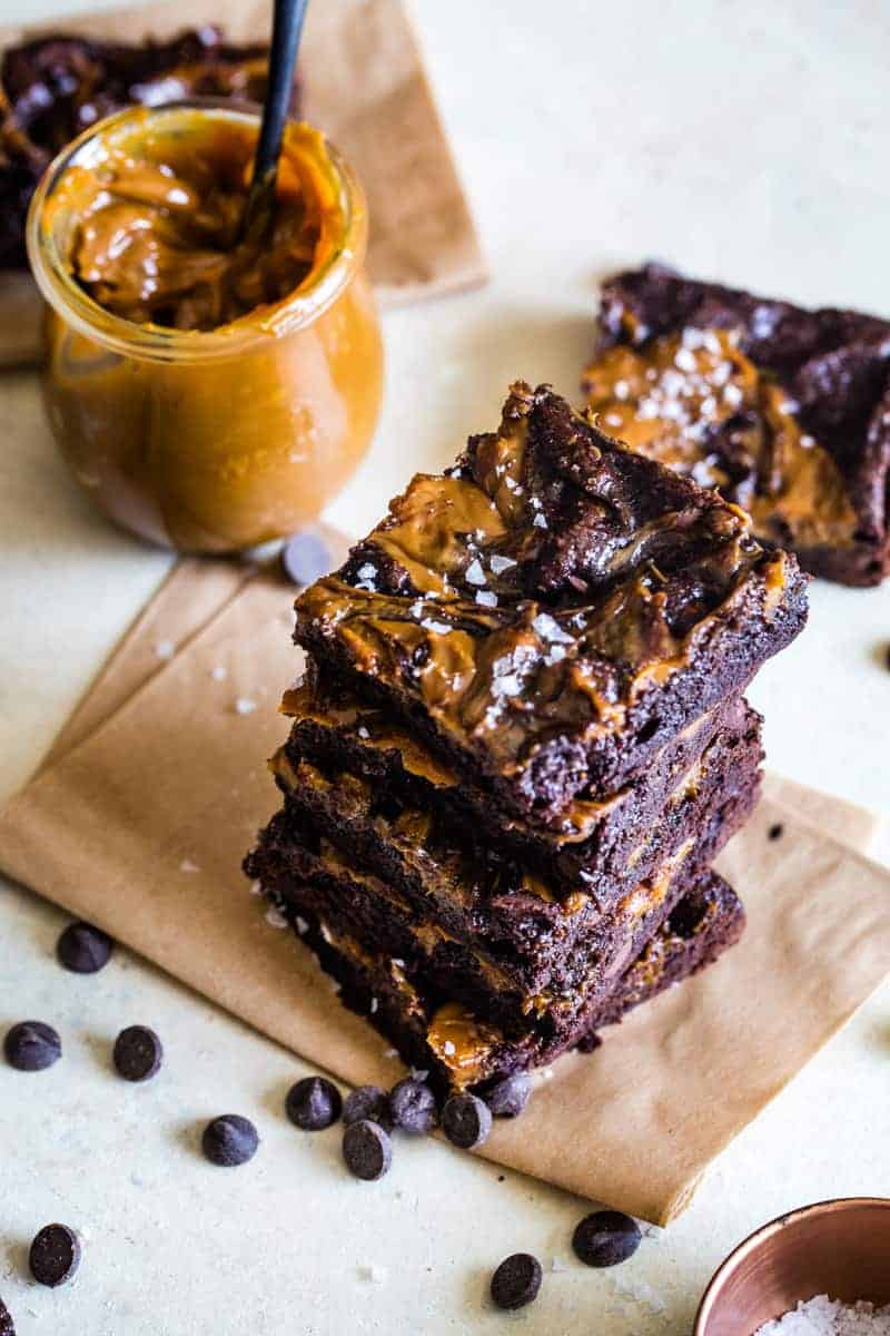 Stack of brownies on a piece of parchment paper and a jar of dulce de leche. 
