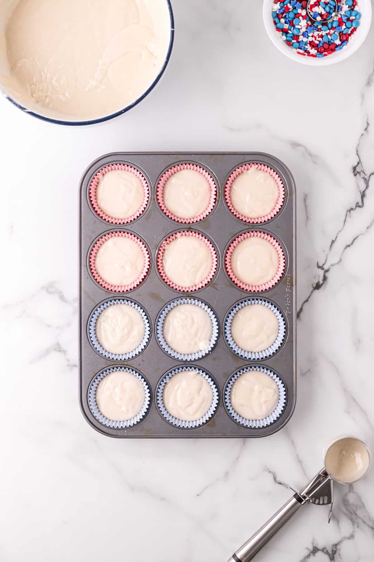 Cupcake batter in red and blue liners in muffin tin. 
