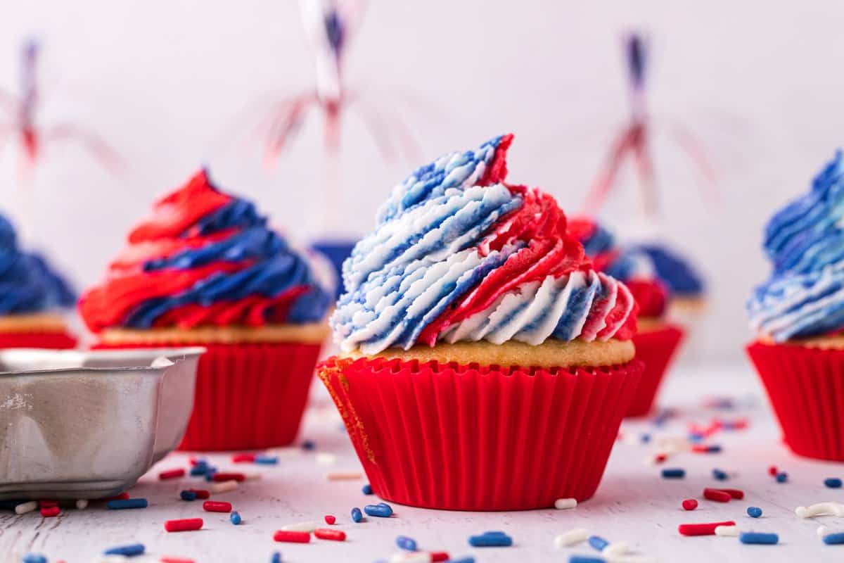 Red white and blue frosted cupcakes in red liners on white background. 