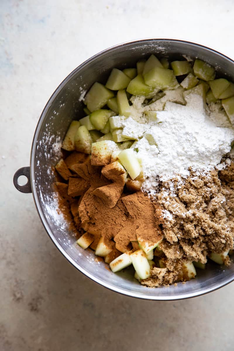 Apple chunks, brown sugar, cornstarch, and cinnamon in large metal mixing bowl.