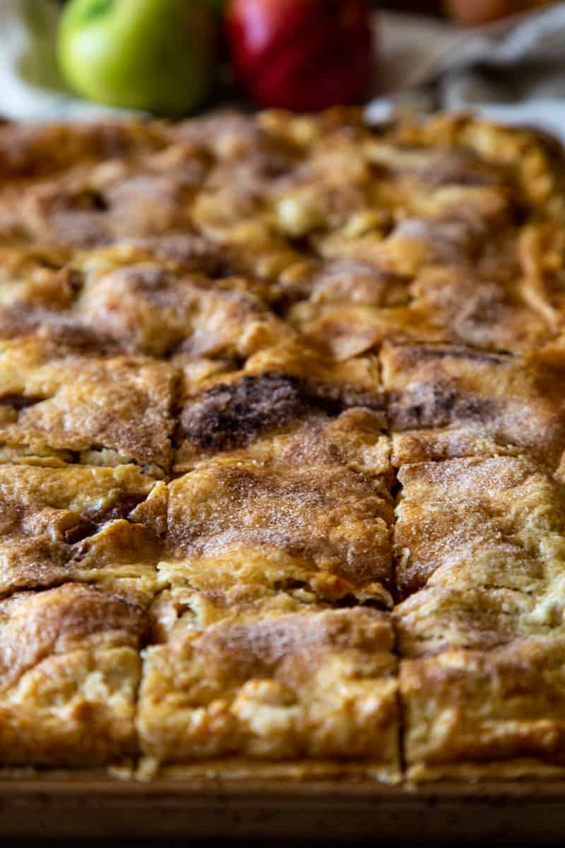 Apple slab pie cut into squares in pan with whole apples in background. 