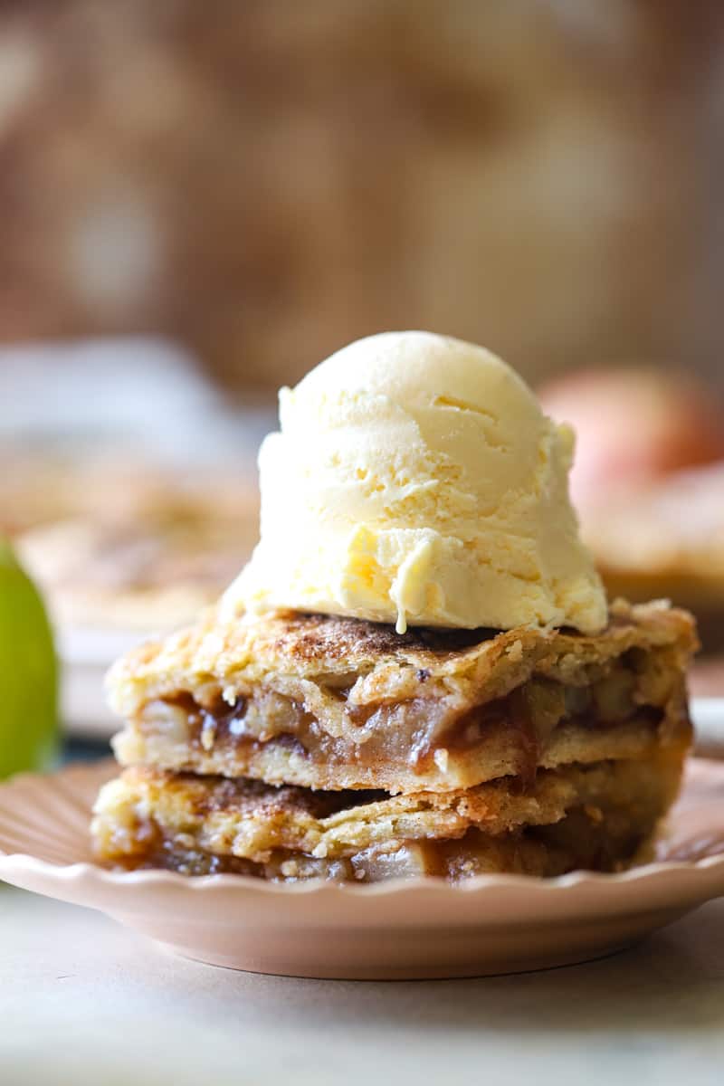 two apple pie squares stacked on pink plate with school of ice cream. 