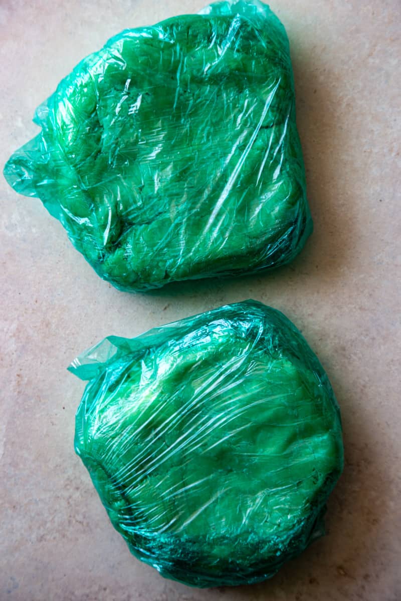 Two pie dough disks wrapped in green plastic wrap. 