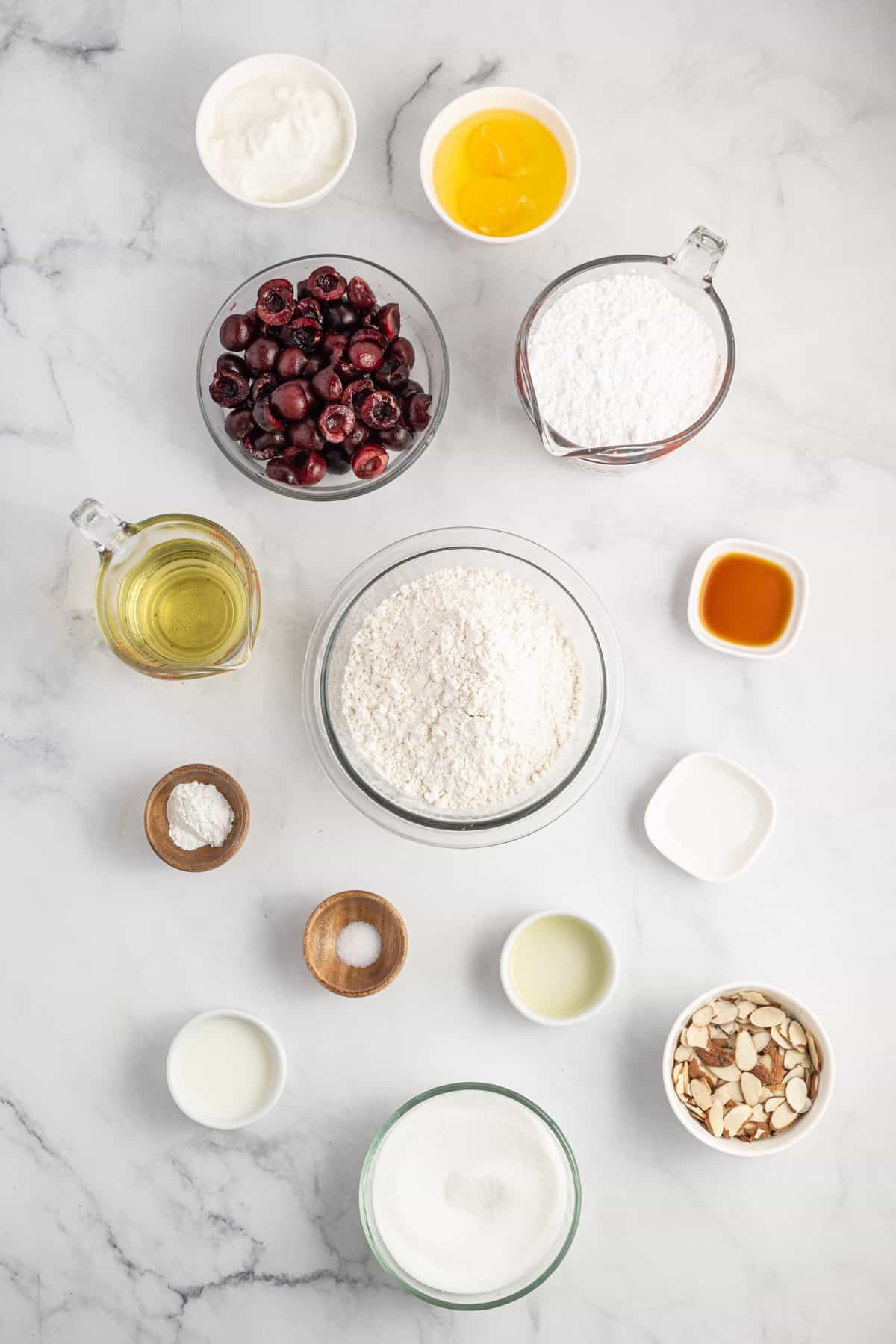 All the ingredients to make cherry bread in little bowls on white background.